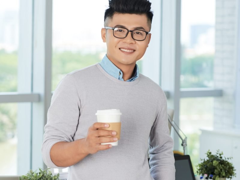 Portrait of young businessman in eyeglasses drinking coffee at office