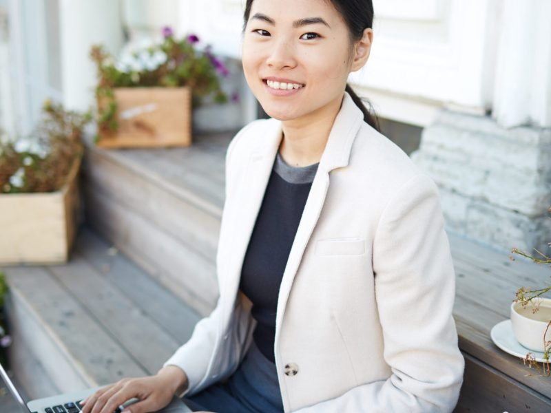 Young Asian female with laptop sitting on stairs in urban environment